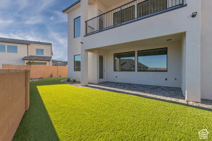 Expansive backyard featuring artificial turf, a paved patio, and a second-story balcony with metal railings