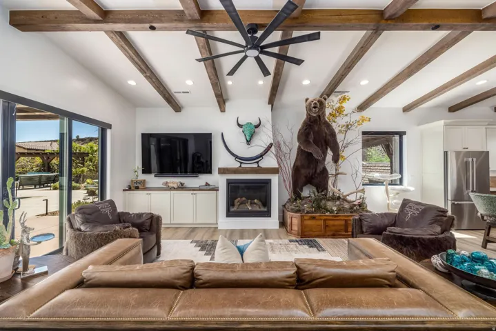 Living area featuring exposed wood beams, recessed lighting, a modern ceiling fan, and a fireplace with a wood-finish mantel
