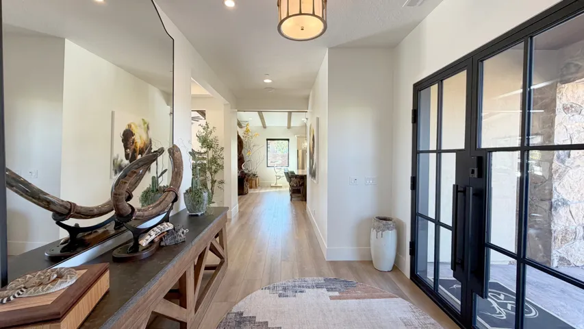 Expansive entryway featuring light wood-finish flooring, a contemporary black-framed glass door, recessed lighting, and a decorative ceiling fixture