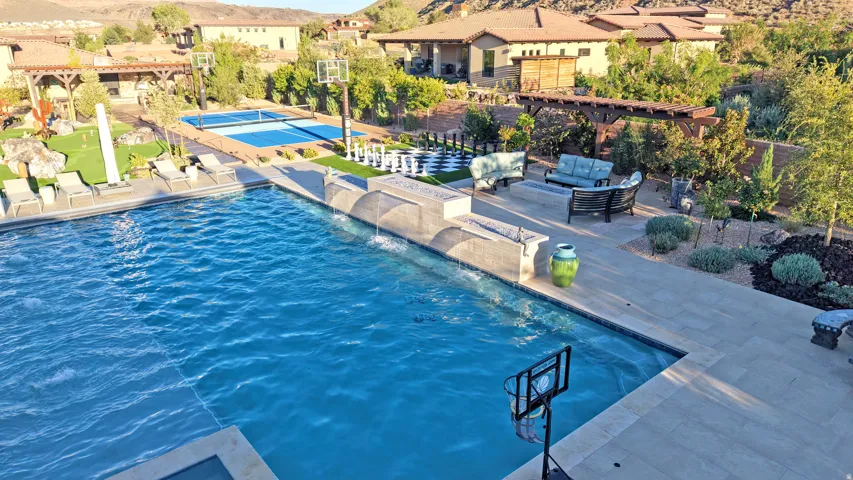 Swimming pool with integrated water features, stone patio, adjacent outdoor lounge area, pickleball court, and manicured landscaping