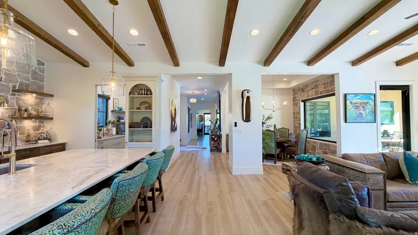 Vaulted ceiling with exposed wood beams, stone accent wall, recessed lighting, wood-finish flooring, and built-in shelving