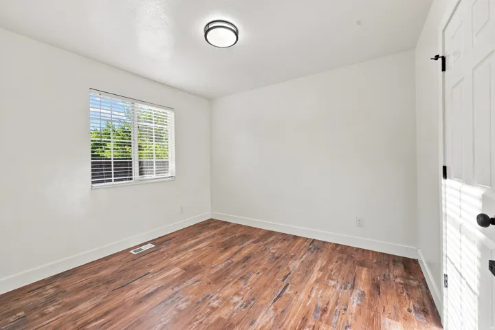 Wood-finish flooring, white walls, window with blinds, flush mount ceiling light, and a paneled door with black hardware