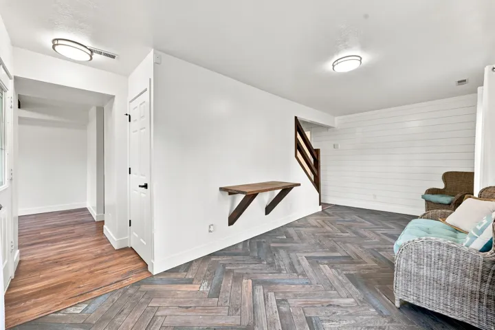 Herringbone pattern wood-finish flooring, white shiplap accent wall, white interior doors with matte black hardware, and a built-in wood-finish shelf