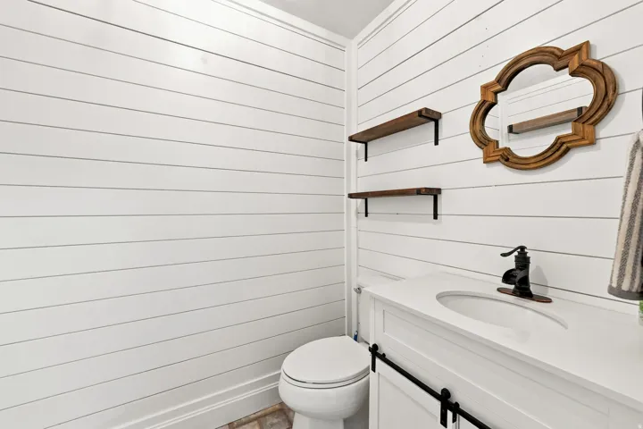 White shiplap walls, white vanity with integrated sink, dark bronze faucet, and wood-finish floating shelves