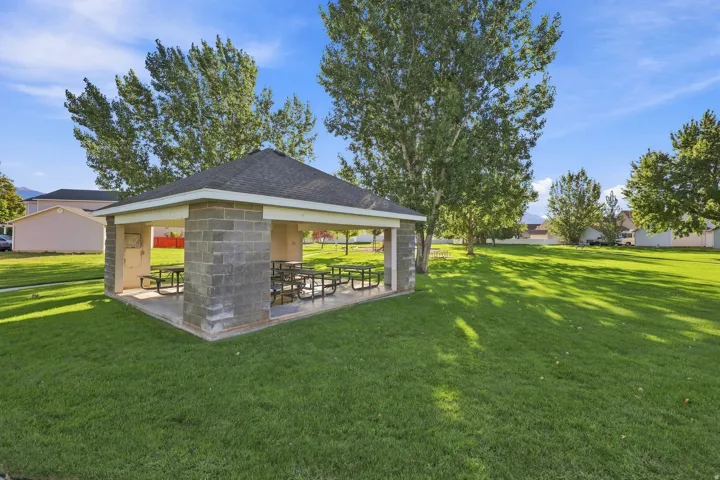 Gazebo with a shingled roof and concrete block construction, situated on a large grassy area with mature trees