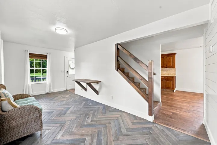 Herringbone-patterned wood-finish flooring, wood staircase with railing, white interior walls, recessed lighting, and a built-in wood shelf