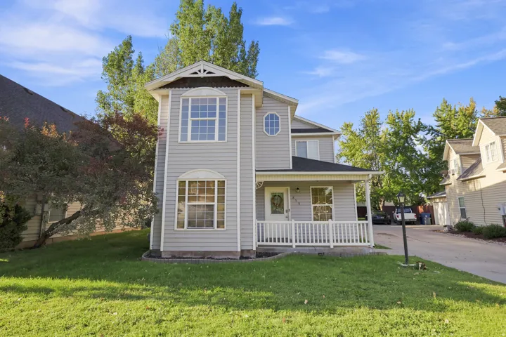 Two-story residence featuring light gray siding, an inviting front porch with white railings, and a prominent bay window
