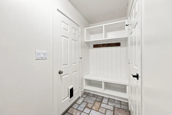 Built-in storage bench with shelving and coat rack, white paneled doors, and multi-toned tile flooring