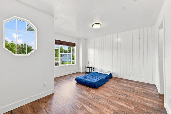 Wood-finish flooring, white shiplap accent wall, octagonal window, recessed window with a brown blind, and ceiling-mounted light fixture