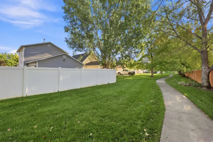 Expansive lawn space with mature trees, a paved walkway, and a white privacy fence