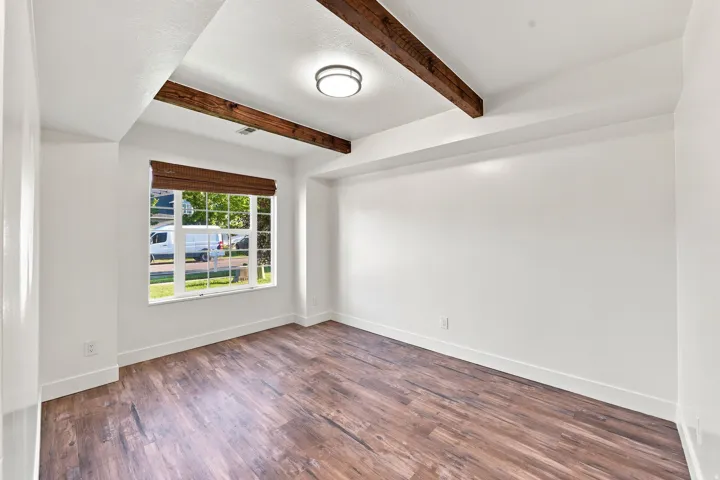 Wood-finish flooring, white walls, exposed wood beams, and a flush-mount ceiling light fixture