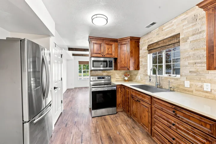 Stainless steel appliances, wood-finish flooring, stone tile backsplash, white countertops, and wood cabinetry