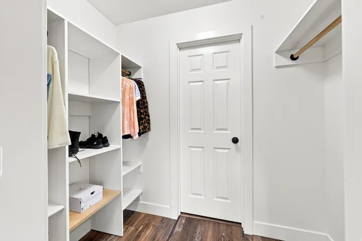 Built-in closet system featuring white shelving, integrated hanging rods, and wood-finish flooring