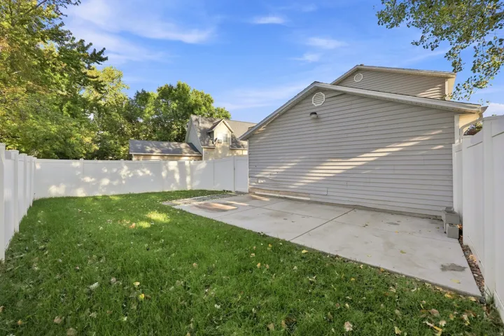 Expansive backyard featuring a manicured lawn, white privacy fencing, and a concrete patio