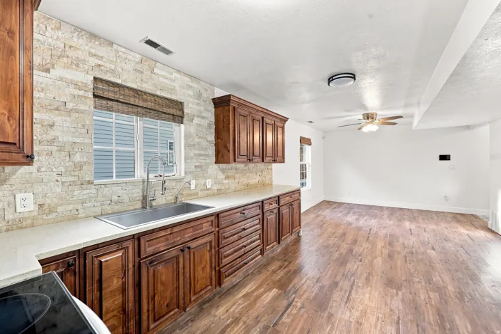 Kitchen area featuring wood-finish flooring, stone-tiled backsplash, ample cabinetry, an undermount sink, and a ceiling fan