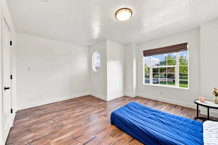 Wood-finish flooring, white walls, flush mount ceiling light, and a prominent window with a woven shade