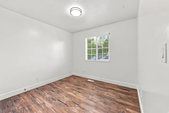 Wood-finish flooring, white walls, window with blinds, and a ceiling-mounted light fixture