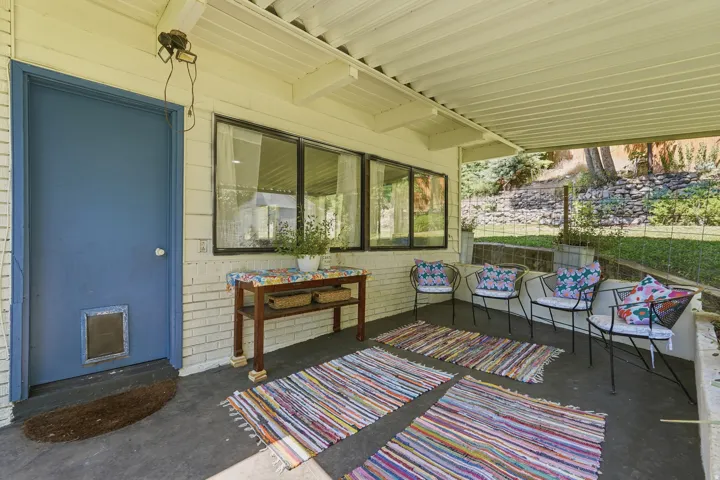 Covered outdoor patio with a solid roof, white painted brick wall, and dark-framed windows