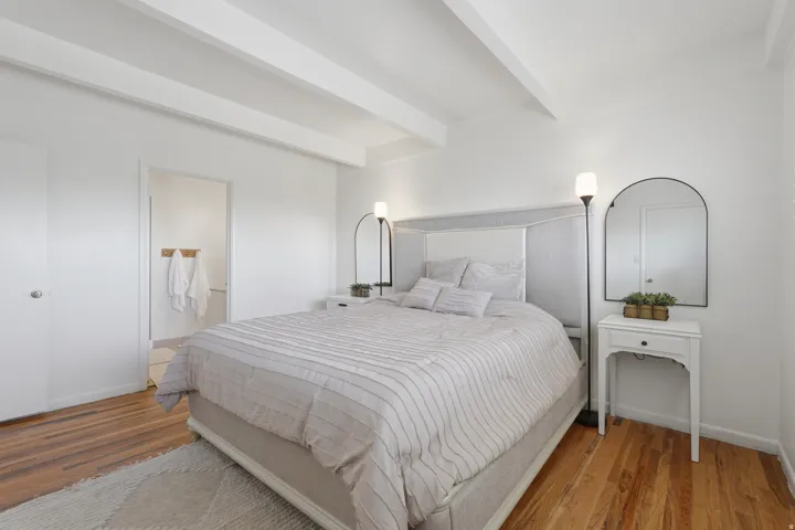 Primary bedroom.  Exposed ceiling beams, wood-finish flooring, and white walls