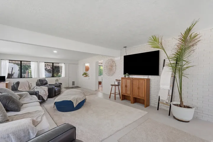 White-painted brick accent wall, recessed lighting, expansive carpeted flooring, large windows, and a wall-mounted media console