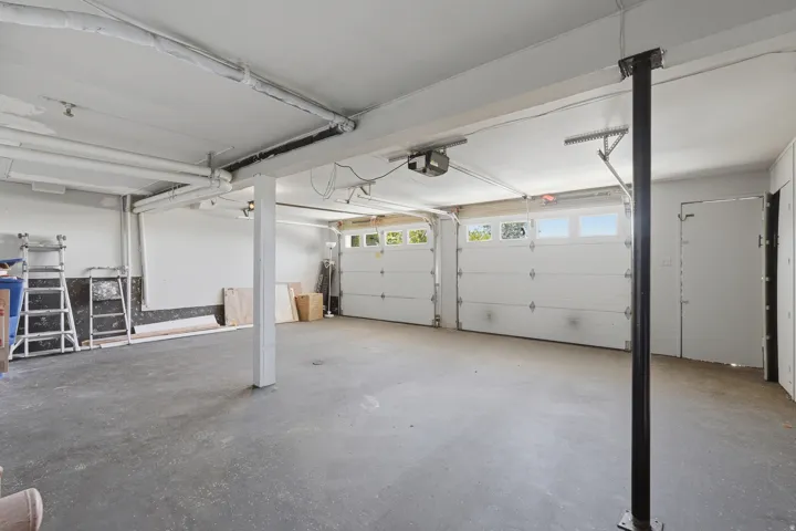 Two overhead garage doors with frosted window panels, exposed ceiling utilities, and a concrete floor