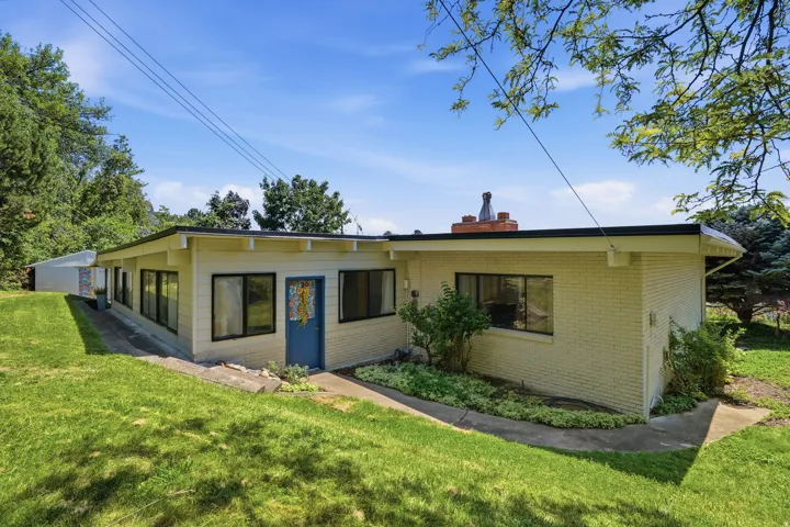 Cream brick exterior with dark trim windows, multiple large windows, and a blue entry door