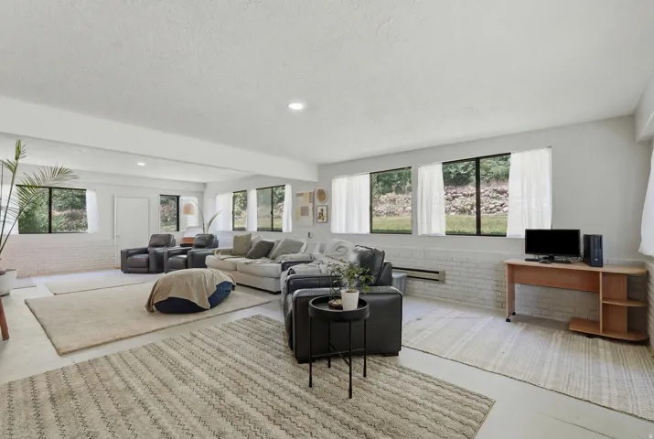 Recessed lighting illuminates this expansive room featuring multiple windows, painted brick accents, and a white ceiling