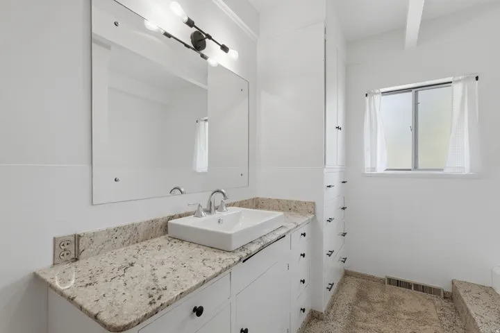 Bathroom #2.  White vanity with a vessel sink and chrome faucet, under-mount lighting, stone-finish countertop, and built-in storage cabinetry