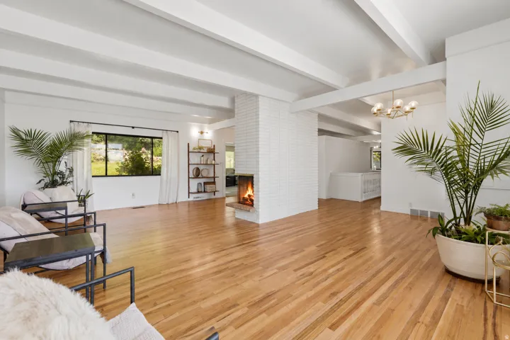 Hardwood flooring, exposed ceiling beams, white brick fireplace, built-in shelving, and a modern chandelier