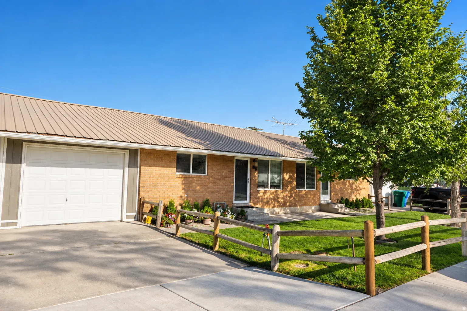 Brick exterior with a brown metal roof, attached garage, and a manicured lawn featuring a wooden fence