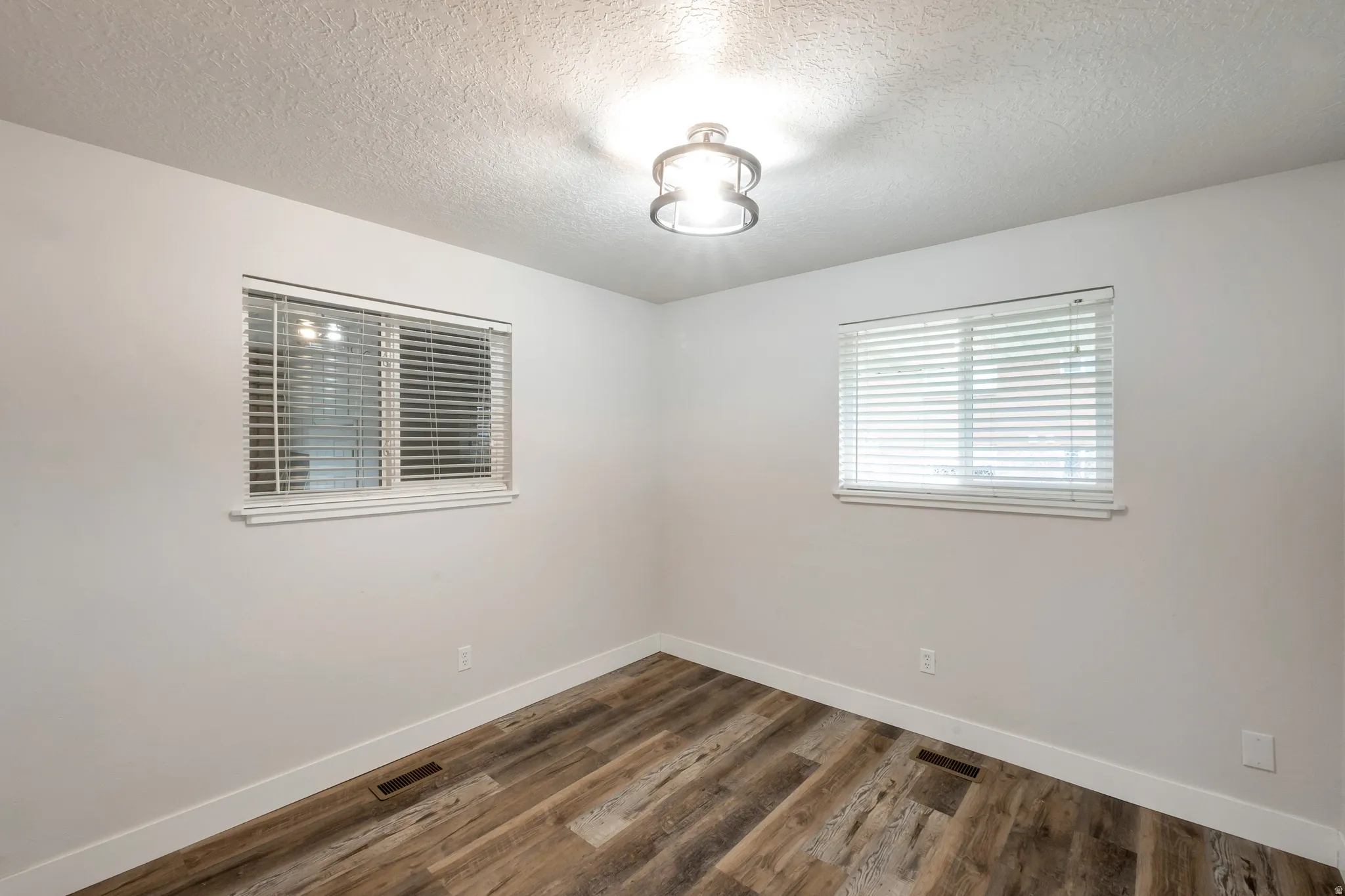 Wood-finish flooring with crisp white trim, two windows with blinds, and a contemporary flush-mount light fixture
