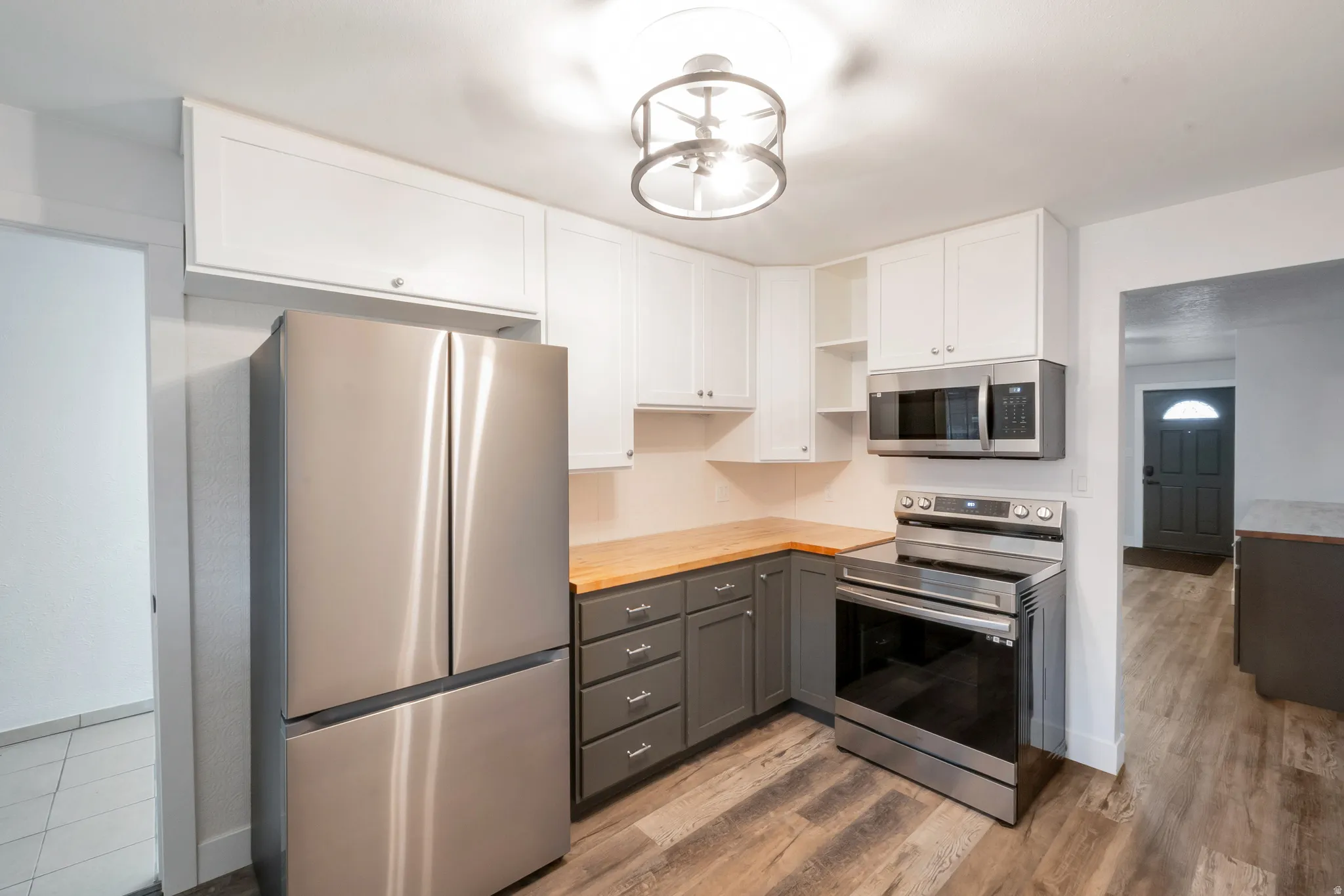 Contemporary kitchen with wood-finish flooring, two-tone cabinetry, stainless steel appliances, and butcher block-style countertops