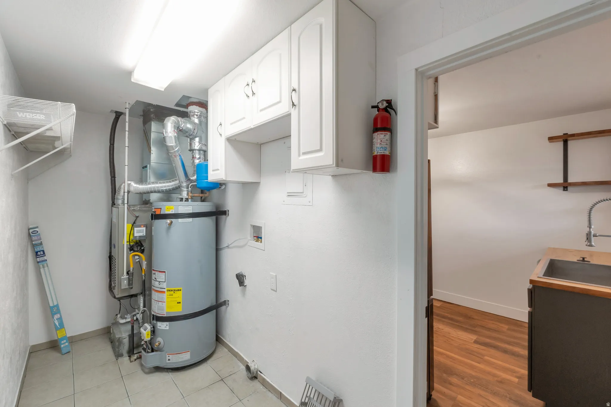 Utility area with tiled flooring, white upper cabinetry, and a ceiling-mounted fluorescent light fixture