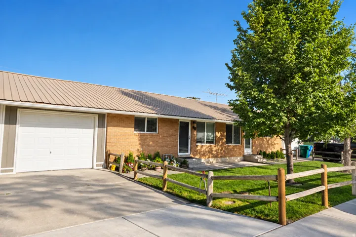 Brick exterior with a brown metal roof, attached garage, and a manicured lawn featuring a wooden fence