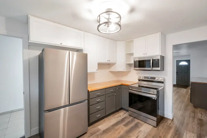 Contemporary kitchen with wood-finish flooring, two-tone cabinetry, stainless steel appliances, and butcher block-style countertops