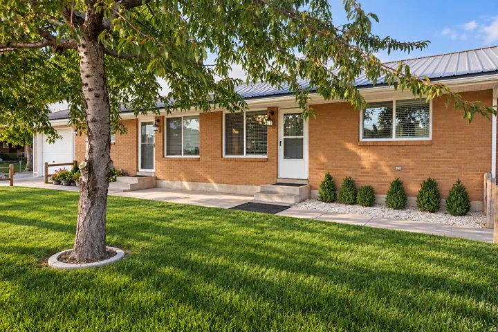 Brick exterior with white trim, a metal roof, and a mature shade tree