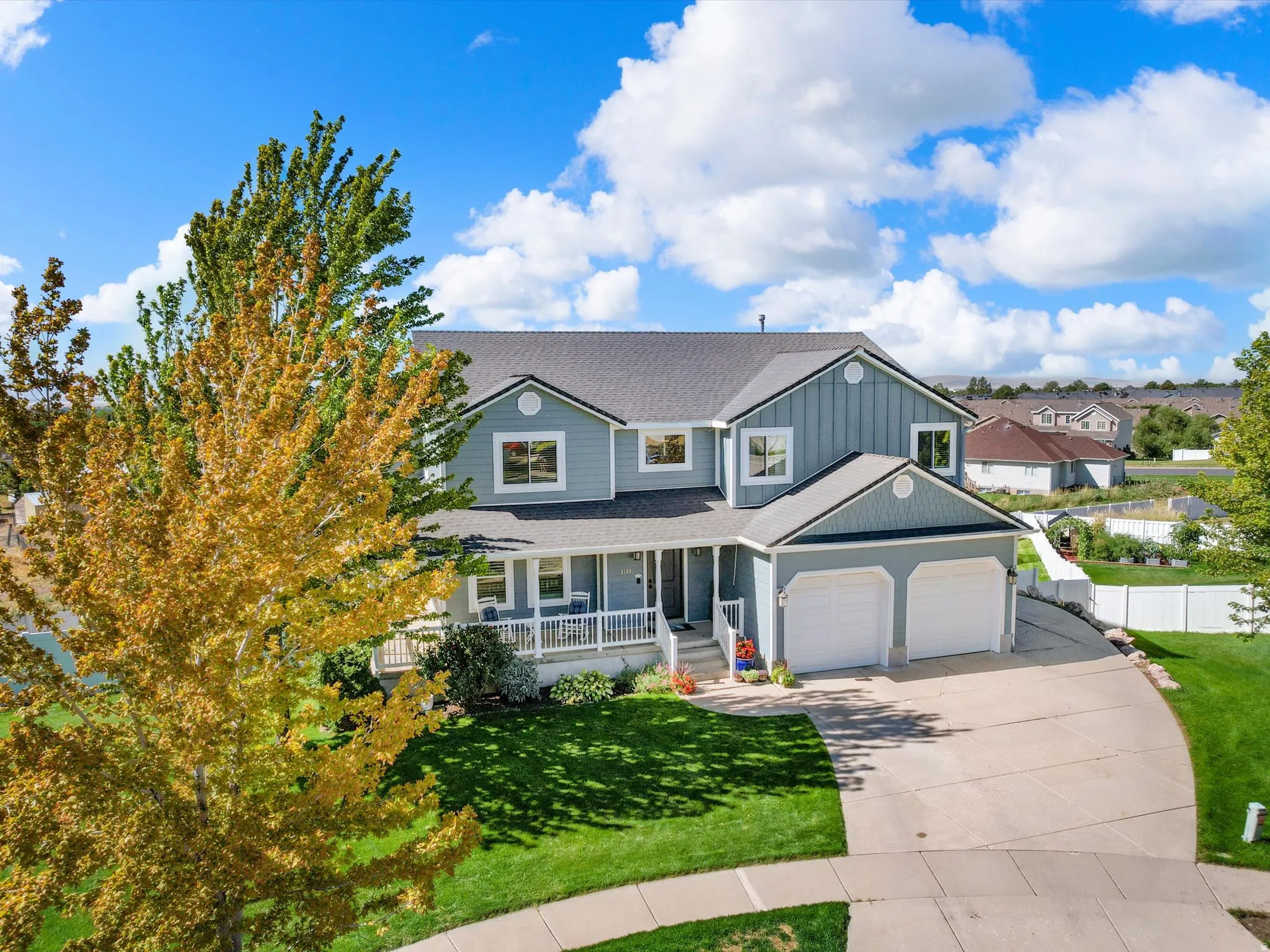 Two-story residence with light blue siding, a dark gray roof, a covered front porch with white railings, a two-car garage, and a concrete driveway