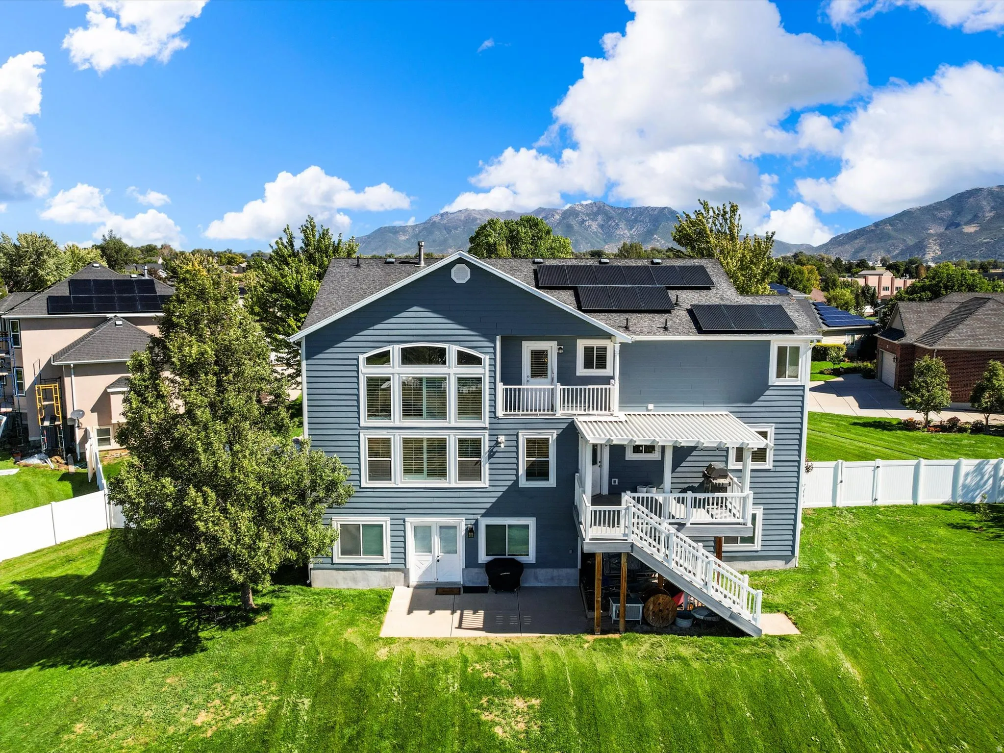Blue siding exterior with multiple solar panels, a multi-level deck with white railings, and a lower-level patio