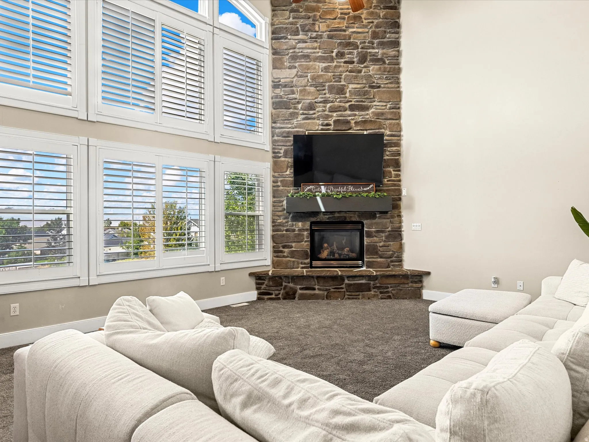 Two-story stone fireplace with a built-in gas fireplace, flanked by a two-story window wall featuring plantation shutters