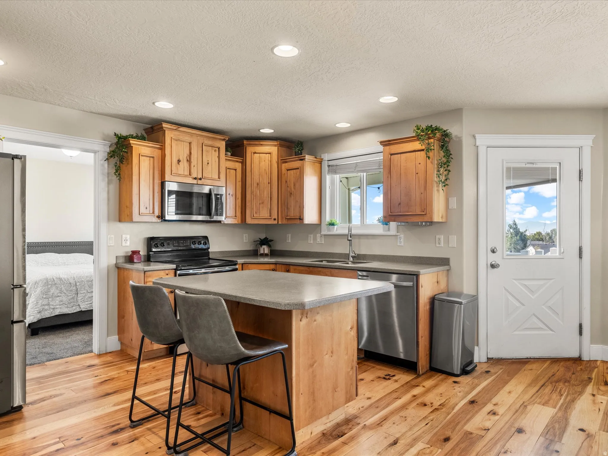 Wood-finish flooring, recessed lighting, wood cabinetry, stainless steel appliances, and a kitchen island with seating