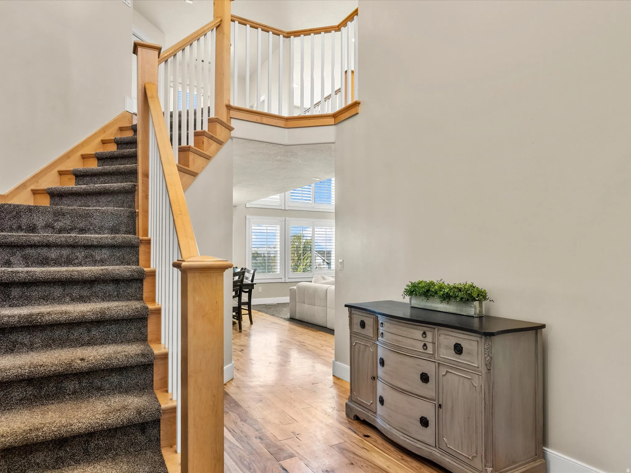 Hardwood flooring, carpeted stairs with wood railing, upper-level balcony, and large windows with plantation shutters