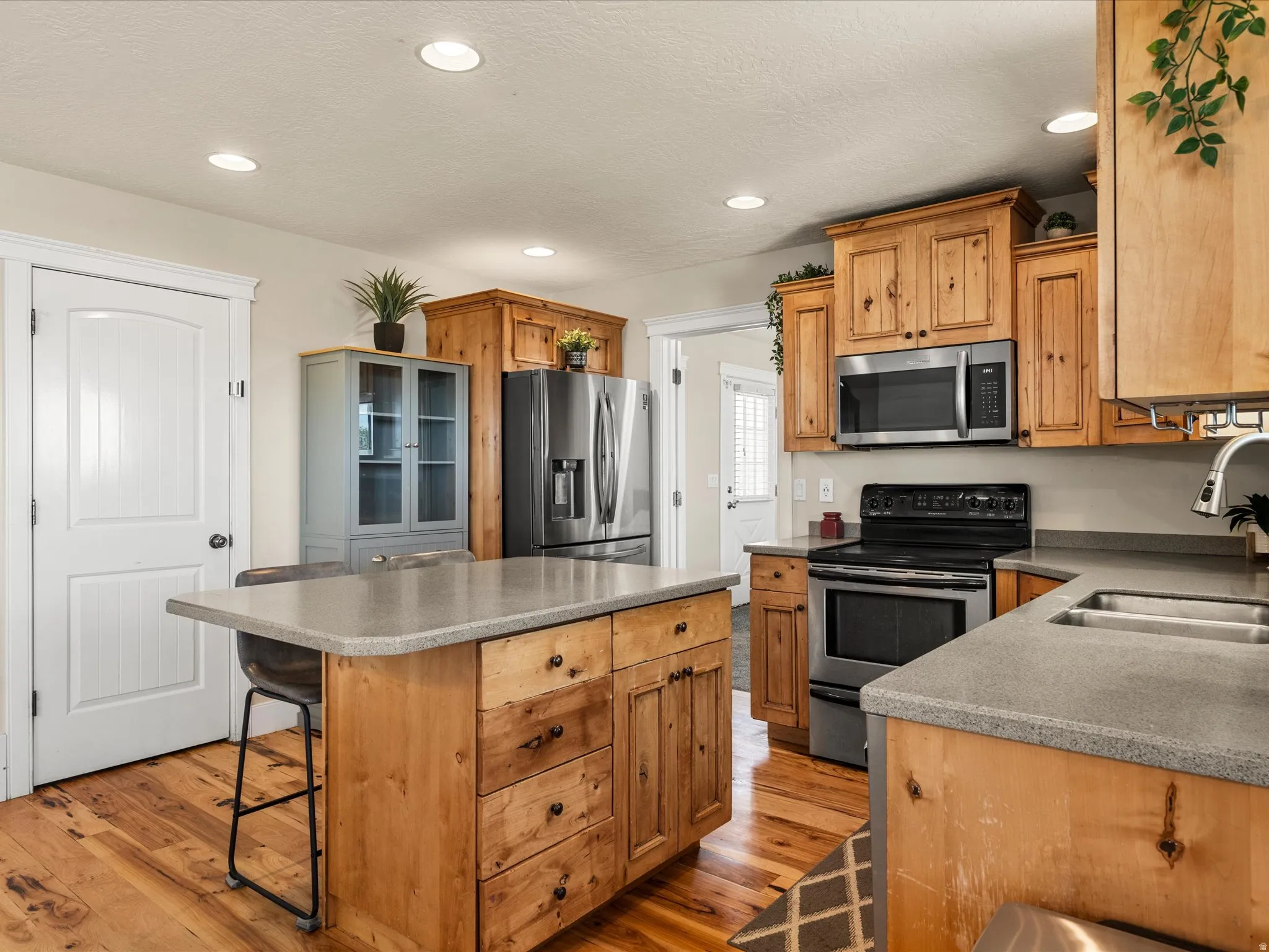 Kitchen featuring wood-finish cabinetry, stainless steel appliances, a center island with a grey countertop, recessed lighting, and wood-finish flooring