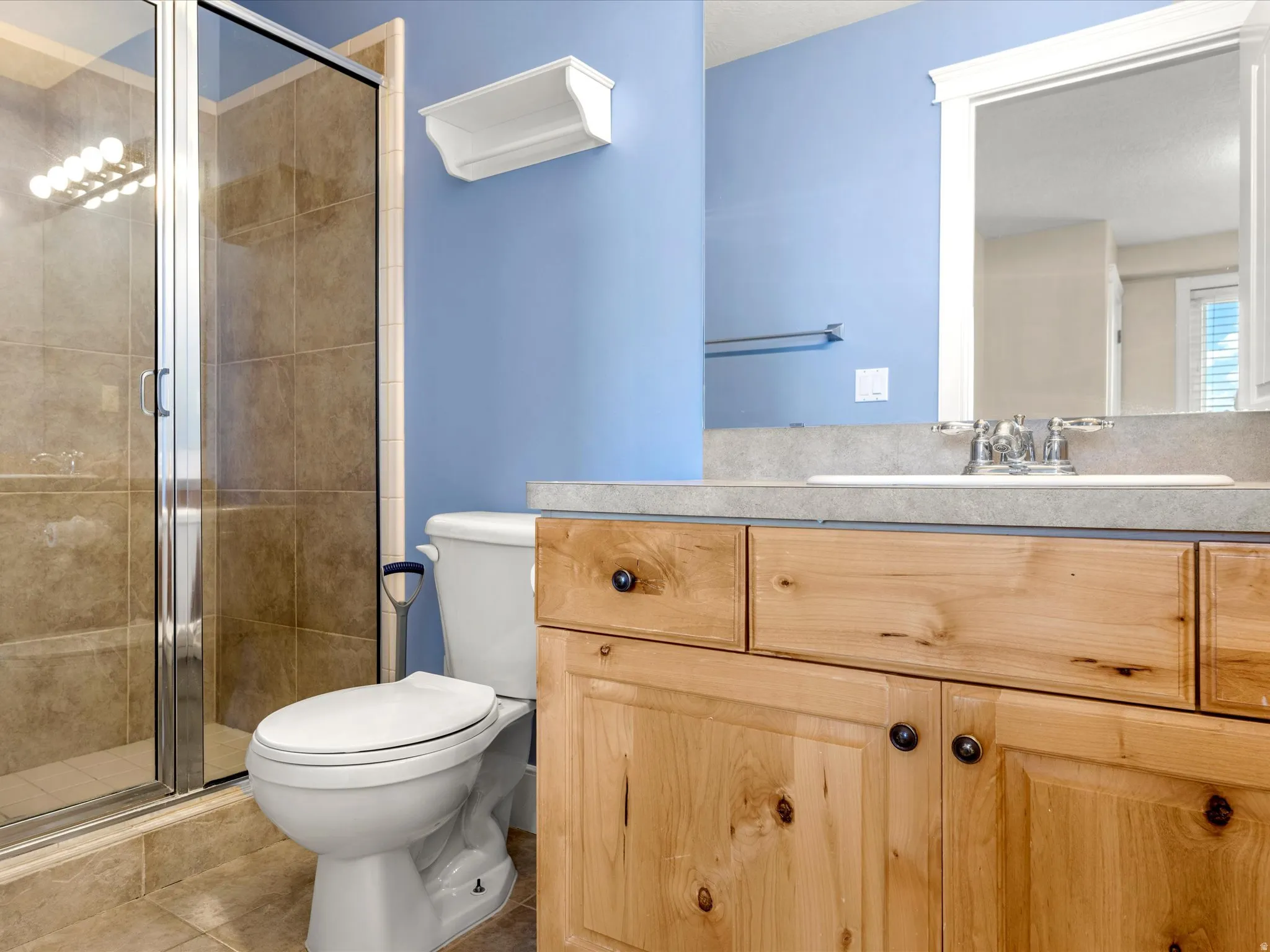 Glass-enclosed shower with tile surround, wood-finish vanity with ample storage, integrated sink, and framed mirror