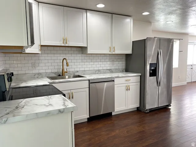 White shaker cabinetry, stainless steel appliances, wood-finish flooring, white subway tile backsplash, and a gold-finish faucet