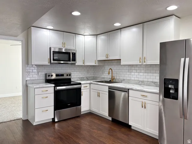 Contemporary kitchen featuring white cabinetry, stainless steel appliances, light-toned countertops, subway tile backsplash, and dark wood-finish flooring