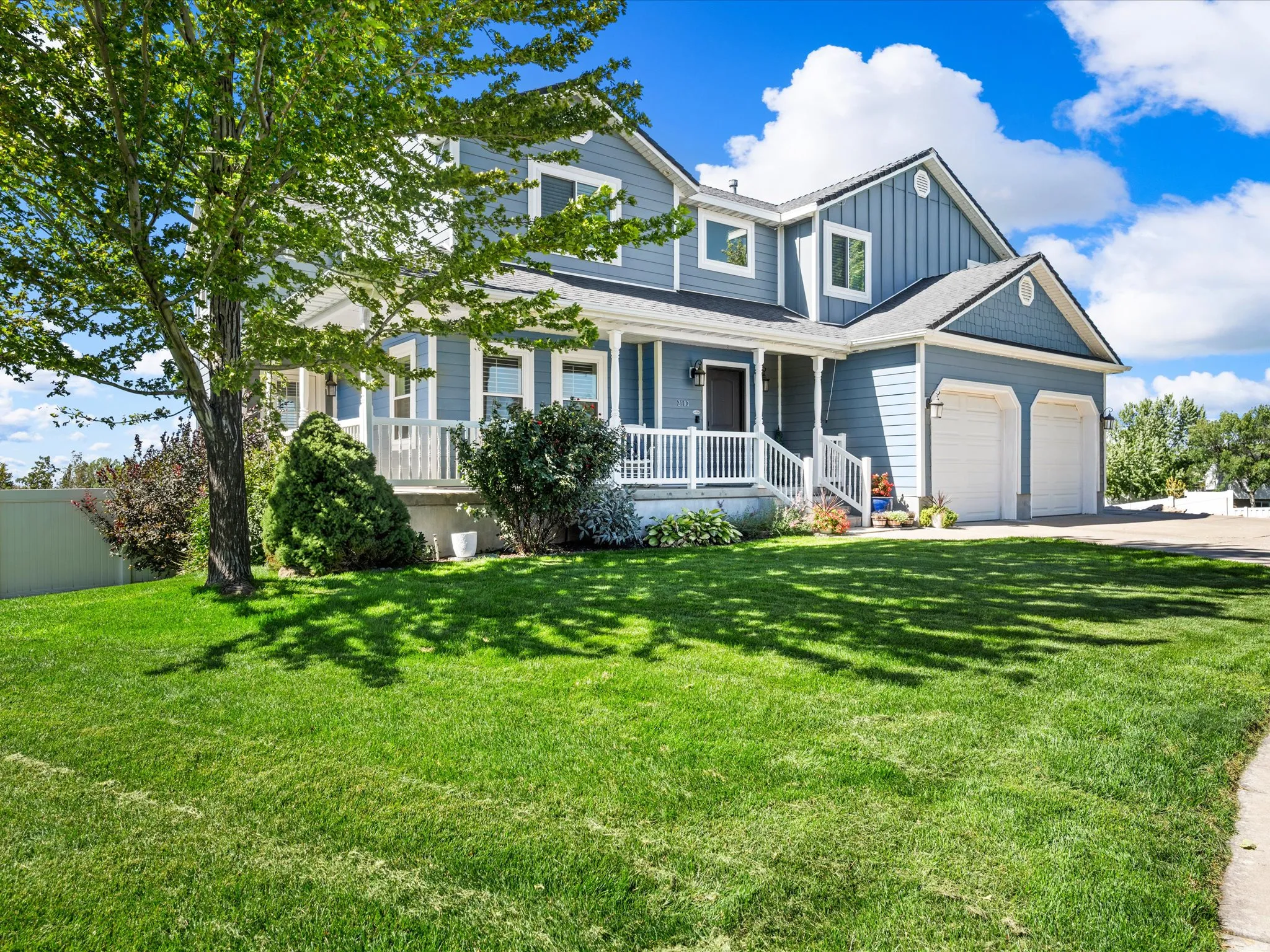Two-story residence featuring light blue siding, a covered front porch with white railings, and an attached two-car garage