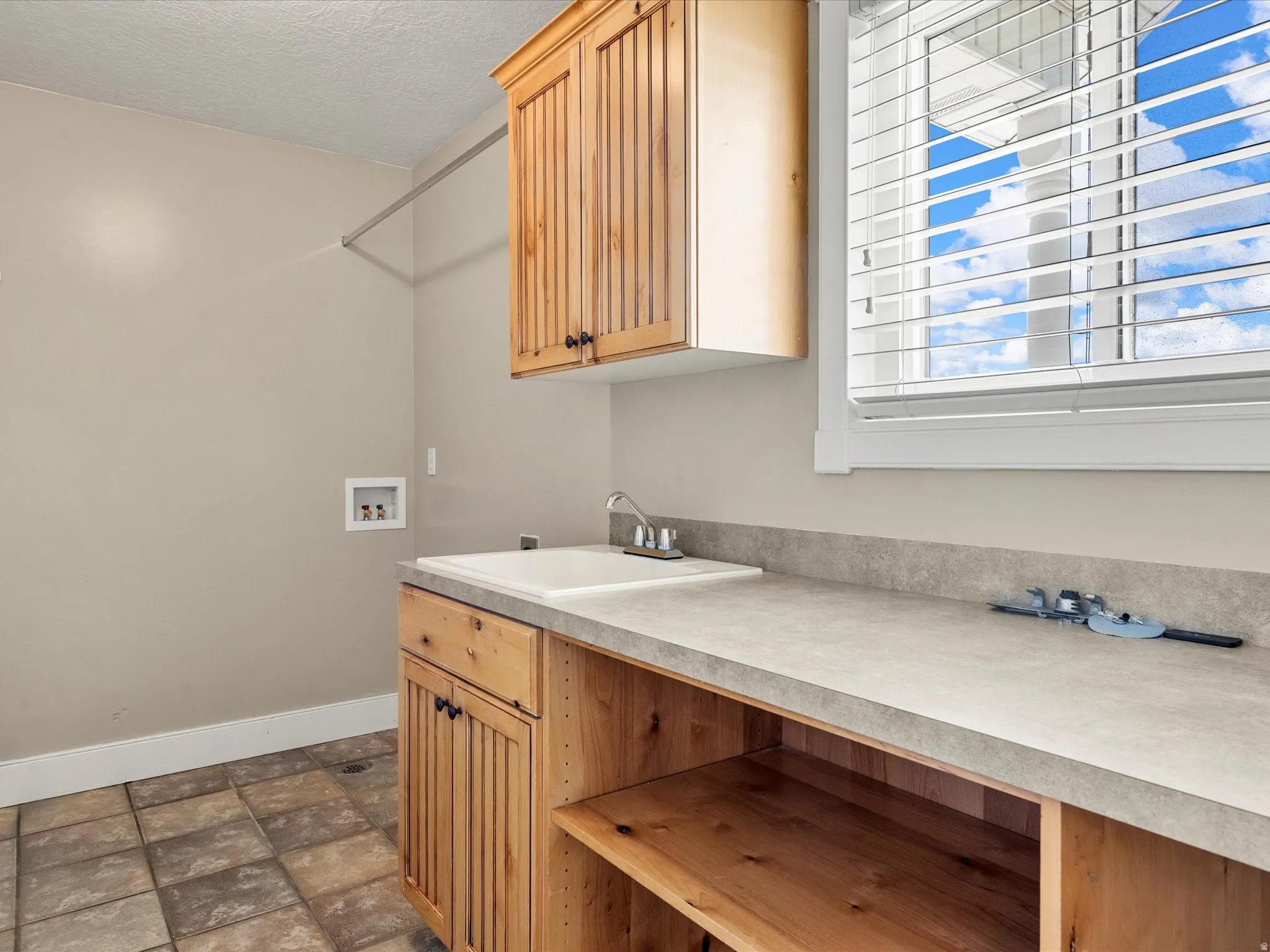 Utility room with wood-finish cabinetry, a built-in sink, and a window with blinds
