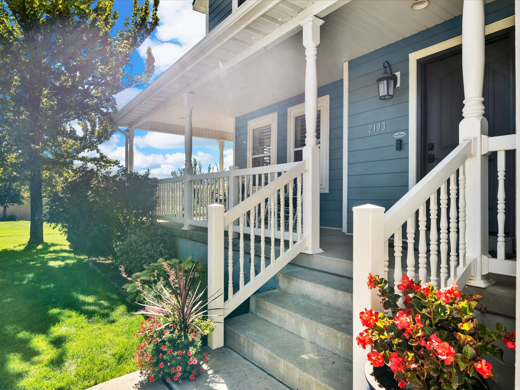 Covered front porch with white railings and balusters, concrete steps, and a blue exterior facade with white trim