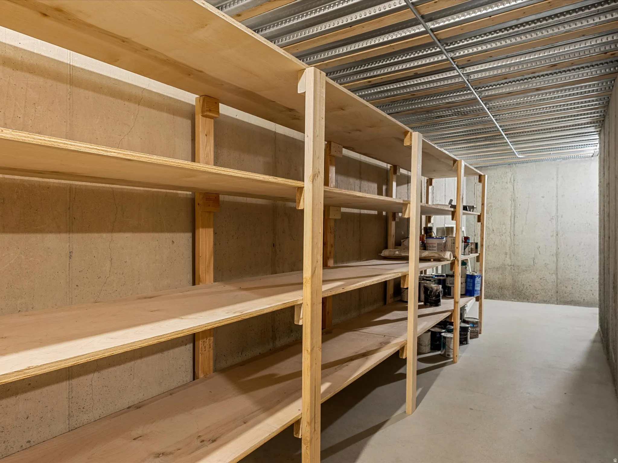 Extensive wood shelving units, concrete walls, concrete flooring, and an exposed metal ceiling