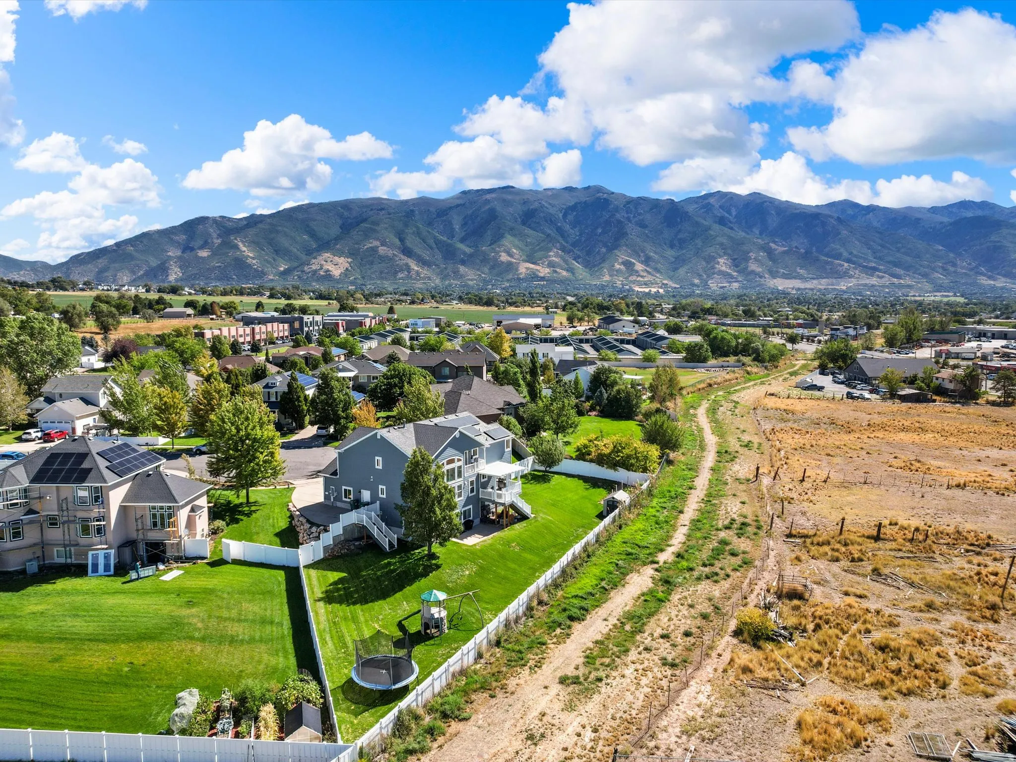 Expansive property featuring a multi-story residence with a gray exterior, a spacious green lawn, a white perimeter fence, and mountain scenery in the background